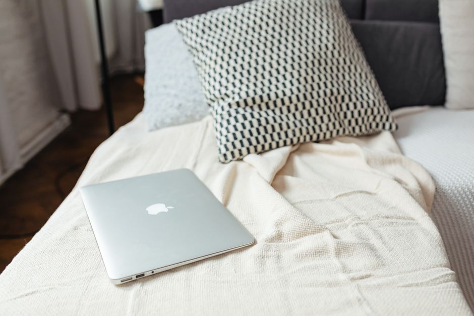 A minimalist scene of a laptop on a textured bed with pillows, capturing a relaxed and modern atmosphere.