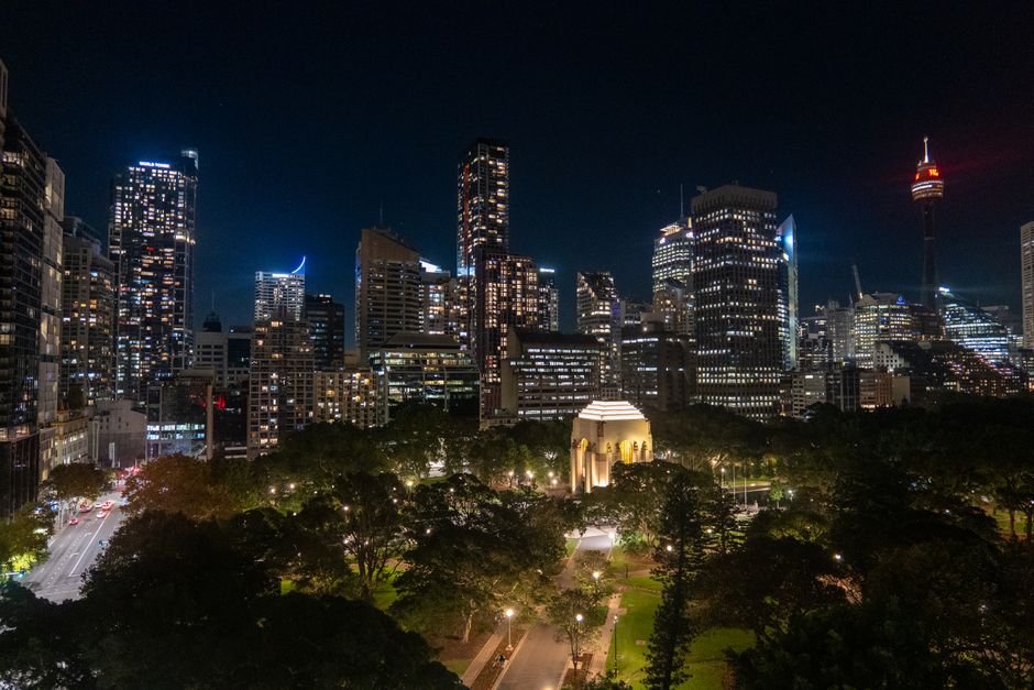 Night view of Sydney's glowing skyline with the illuminated Sydney Tower and Anzac Memorial.