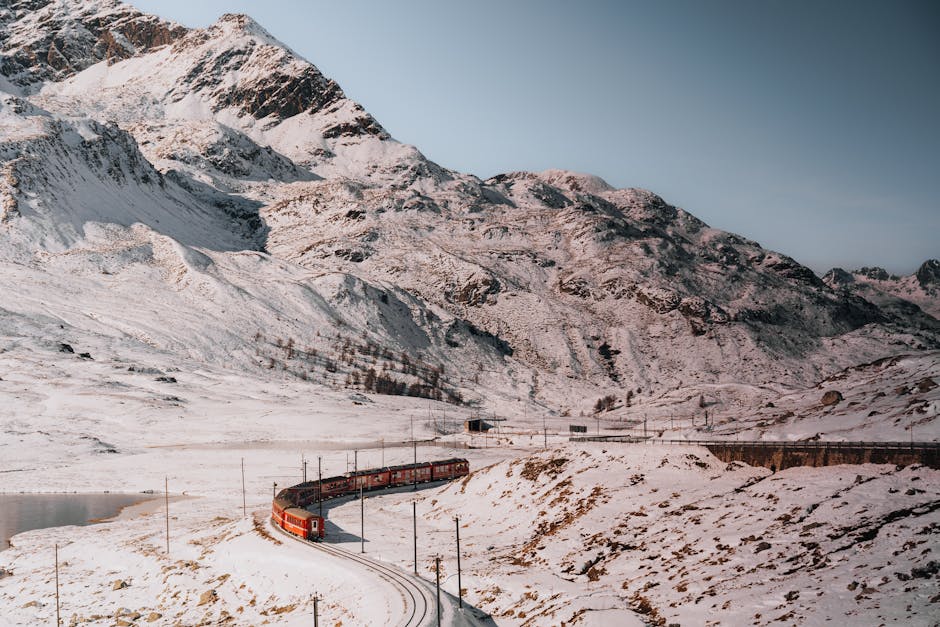 Red train winds through snow-covered mountains, offering breathtaking views of winter scenery.