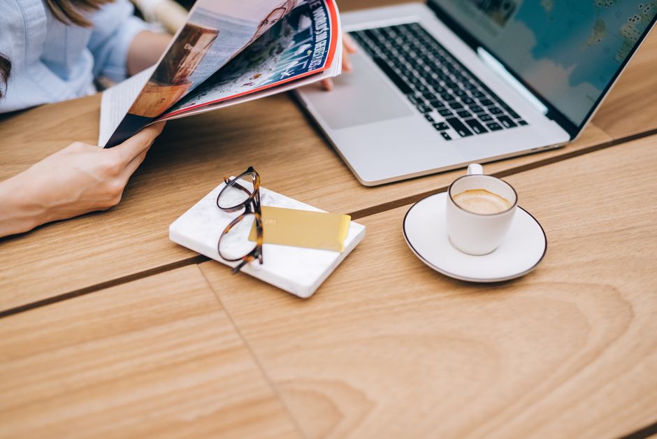 A relaxed workspace featuring a laptop, coffee, and reading materials on a wooden table.