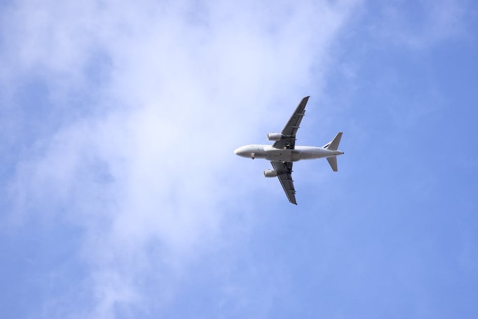 A large commercial jet flying against a backdrop of clear blue sky with scattered clouds.