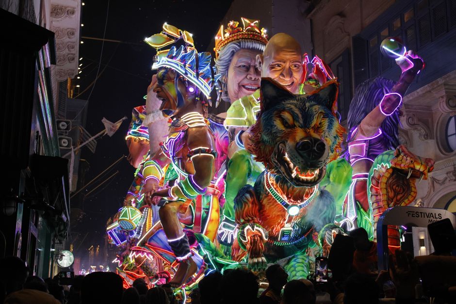 Colorful illuminated parade float featuring oversized carnival figures during nighttime festival celebration.