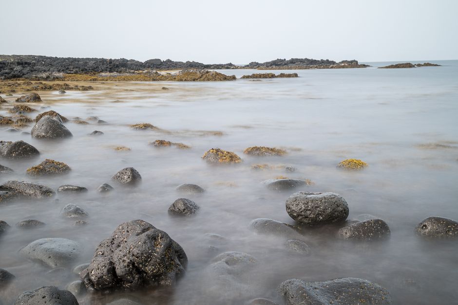 Peaceful seaside landscape with rocks softened by long exposure, creating a serene coastal scene.