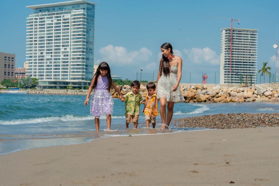A family of four enjoying a sunny day at the beach, playing near the sea with skyscrapers in the background.