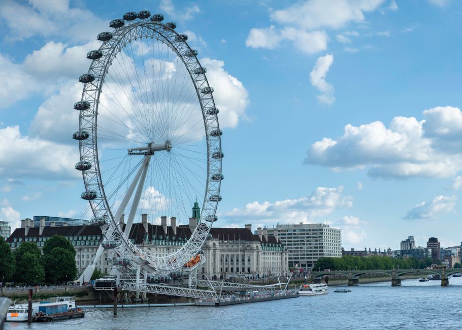 A scenic view of the London Eye by the River Thames under a vibrant blue sky.