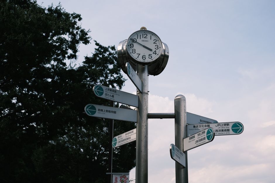 Street clock and signpost in urban setting with directional signs and blue sky.