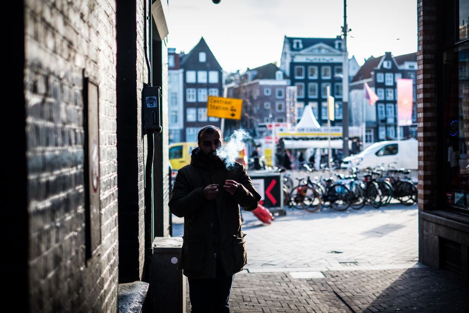 A man smokes in a vibrant Amsterdam street scene with bicycles and architecture.