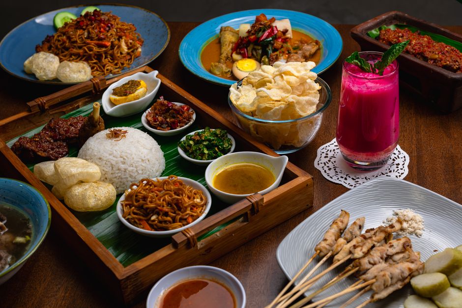 A vibrant spread of traditional Indonesian dishes featuring chicken satay, rice, and colorful side dishes.