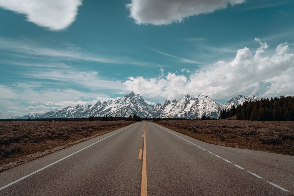 A scenic road leading to snowcapped mountains under a bright blue sky.