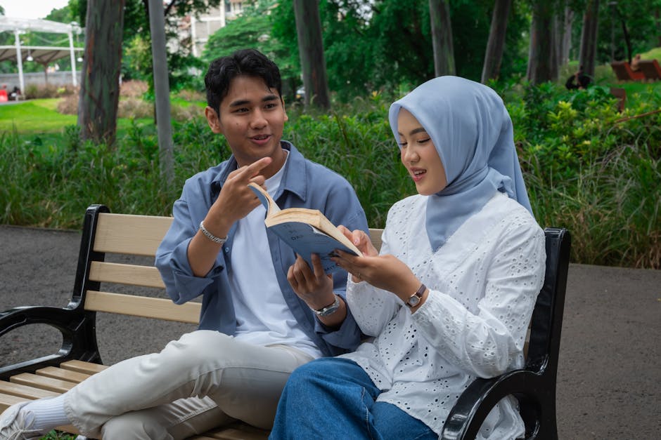 A joyful couple enjoys reading together in an Indonesian park, wearing casual attire.