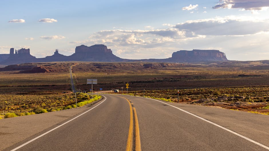 Open road view towards iconic Monument Valley rock formations at sunset.