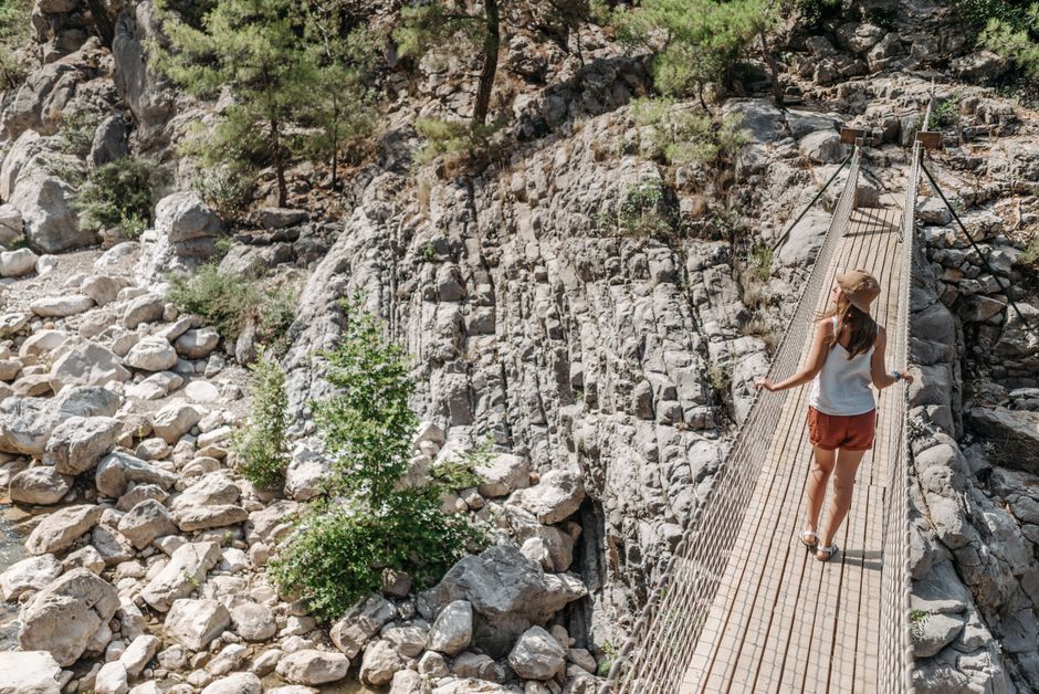 Woman crossing a suspension bridge in a rocky landscape, ideal for adventure and travel themes.
