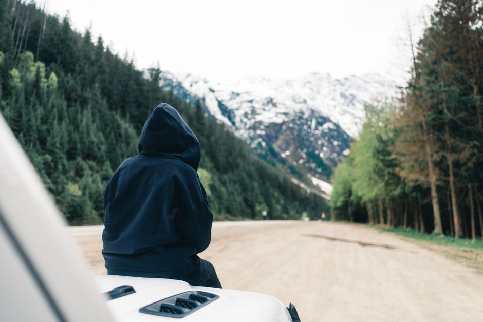 A person in a hoodie enjoys a peaceful moment on a mountain road in British Columbia, Canada.