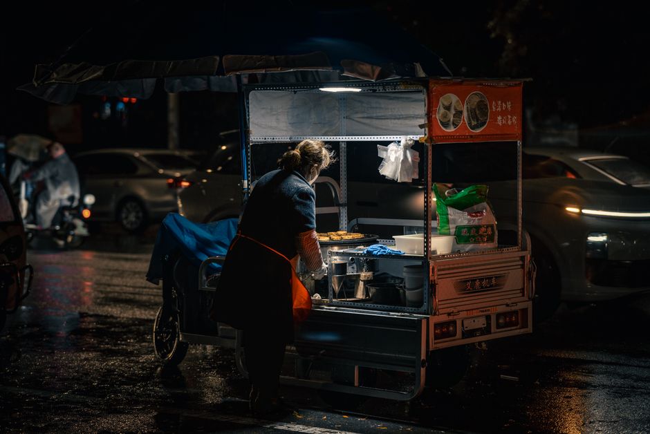 A vendor prepares food in a street cart at night, highlighting urban street food culture.