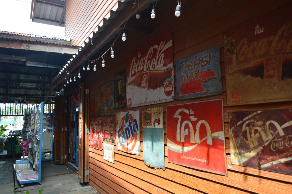 Collection of vintage Coca-Cola and Pepsi signage displayed on a wooden wall in an outdoor market.