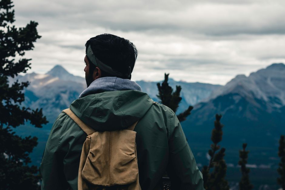 A hiker wearing a green jacket pauses to admire the mountain view in Banff, Alberta, Canada.