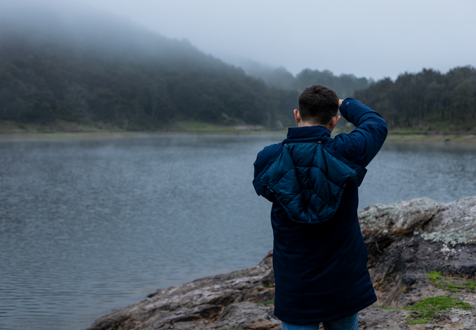 A man in a jacket stands by a foggy lakeshore in Santa Rosa de Lima, Mexico.