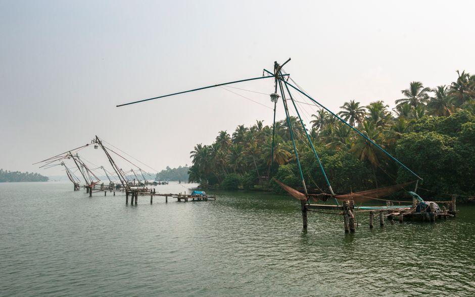 Scenic view of traditional Chinese fishing nets along Kerala backwaters surrounded by lush palm trees.