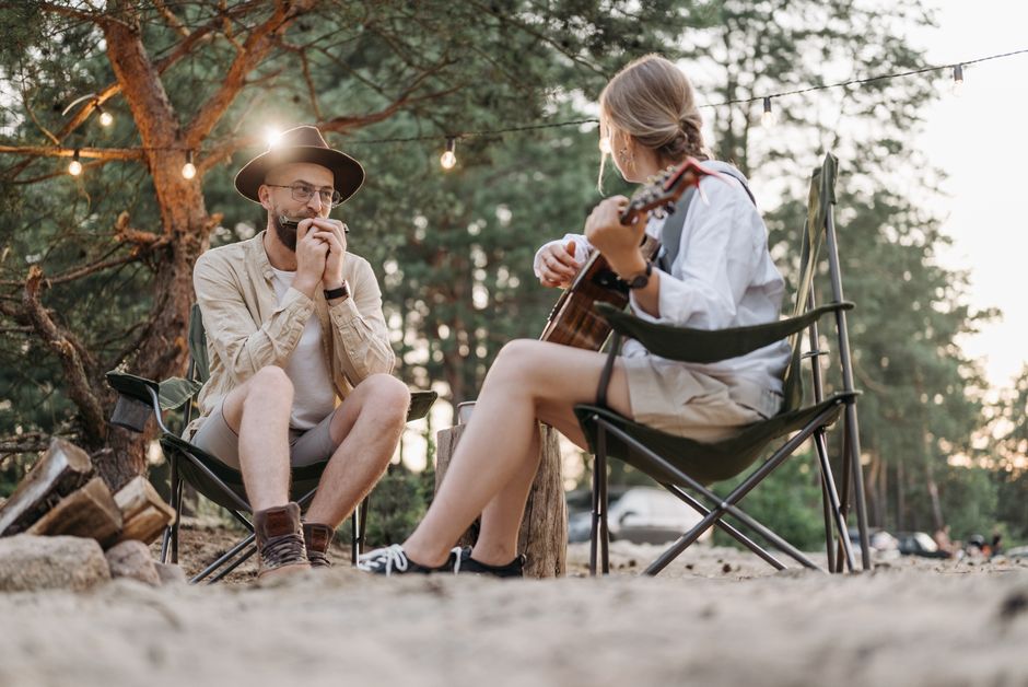 A harmonious moment of a couple playing guitar and harmonica while camping in a tranquil forest setting.