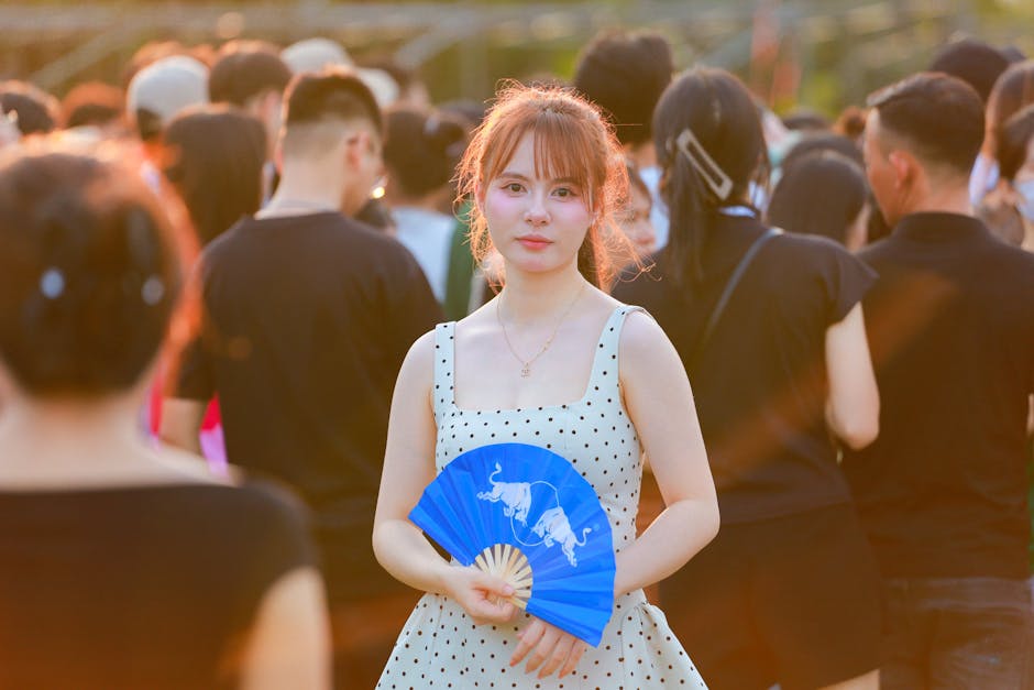 A young woman in a crowd holds a blue fan at a festival in Hà Nội, Việt Nam.